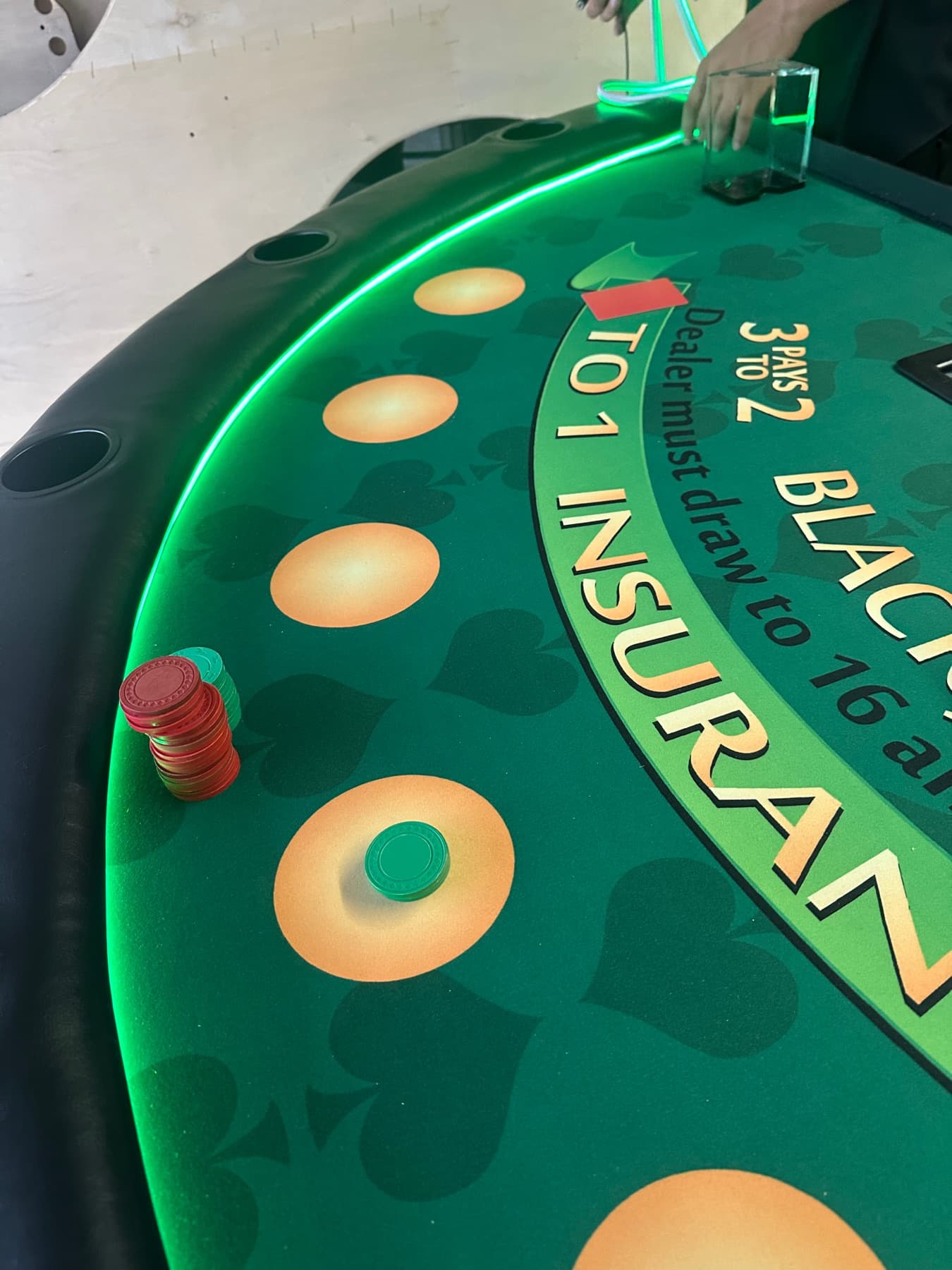 Close-up of a green blackjack felt with its LED rim lit and a stack of chips